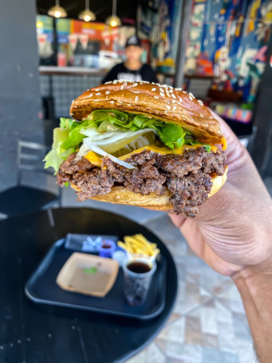 Big Smack da Malta Parrilla segurado na mão, com fritas e bebida ao fundo